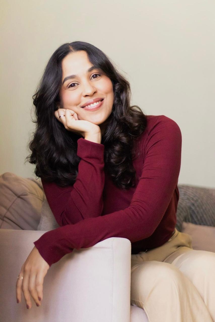 Ana Alves sorrindo, com blusa vinho e a mão apoiada no rosto